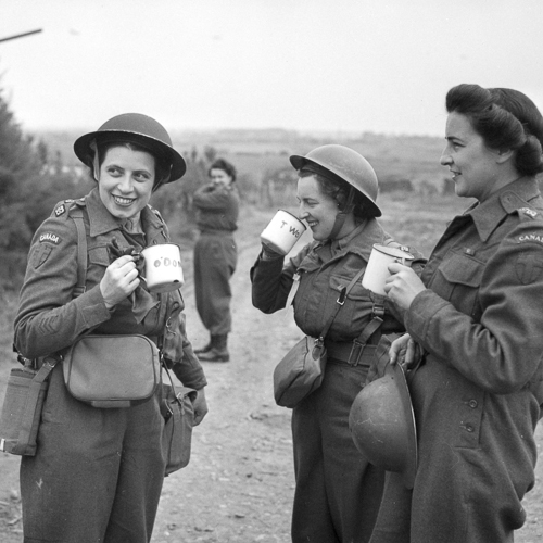 Trois infirmières de l’armée canadienne en tenue de combat et casques Mark II prenant le thé dehors.