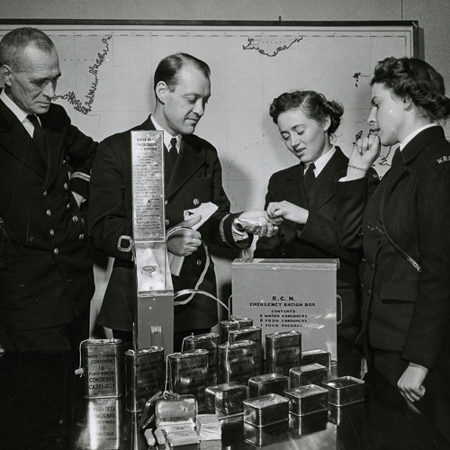 Deux hommes et deux femmes de la marine, déballent et dégustent la ration de chocolat d'un boîte de rationnement.