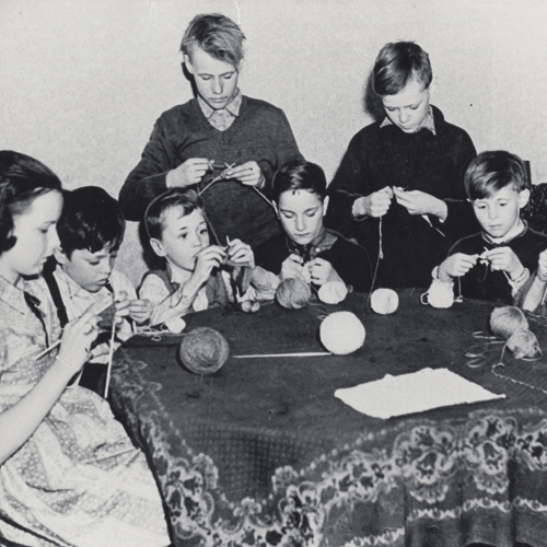 Huit garçons et une fille assis autour d'une table tricotant.