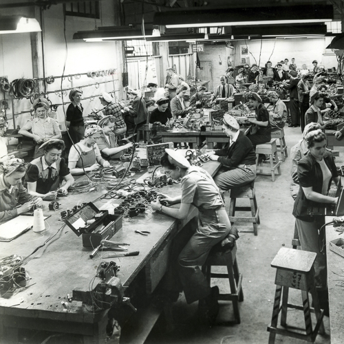 Quelques femmes sur les planchers d'une usine, portent un fichu et d'autres, un chapeau.