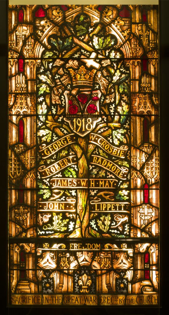 Un vitrail coloré représentant un arbre encadré par un arc gothique.