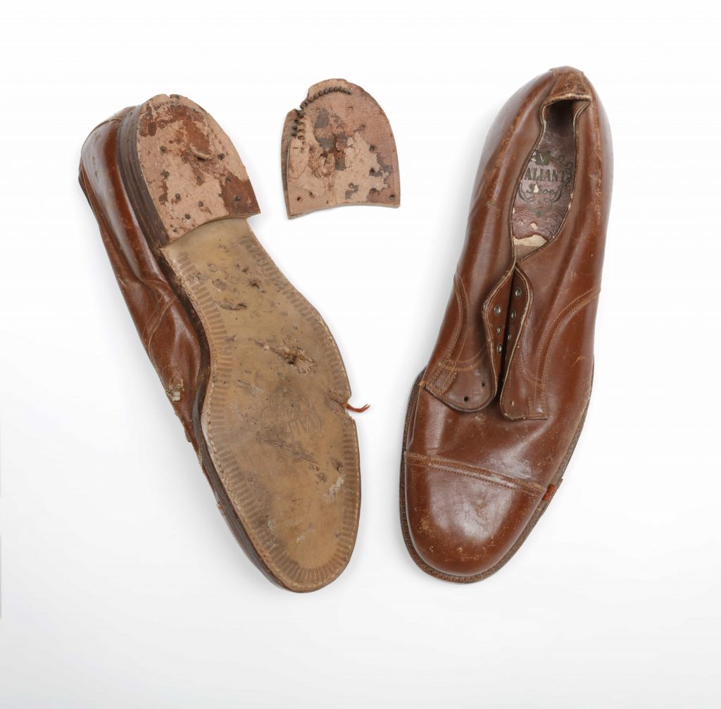 Deux chaussures en cuir marron, dont l’une est à l’envers, montrant une semelle endommagée et un talon détaché.