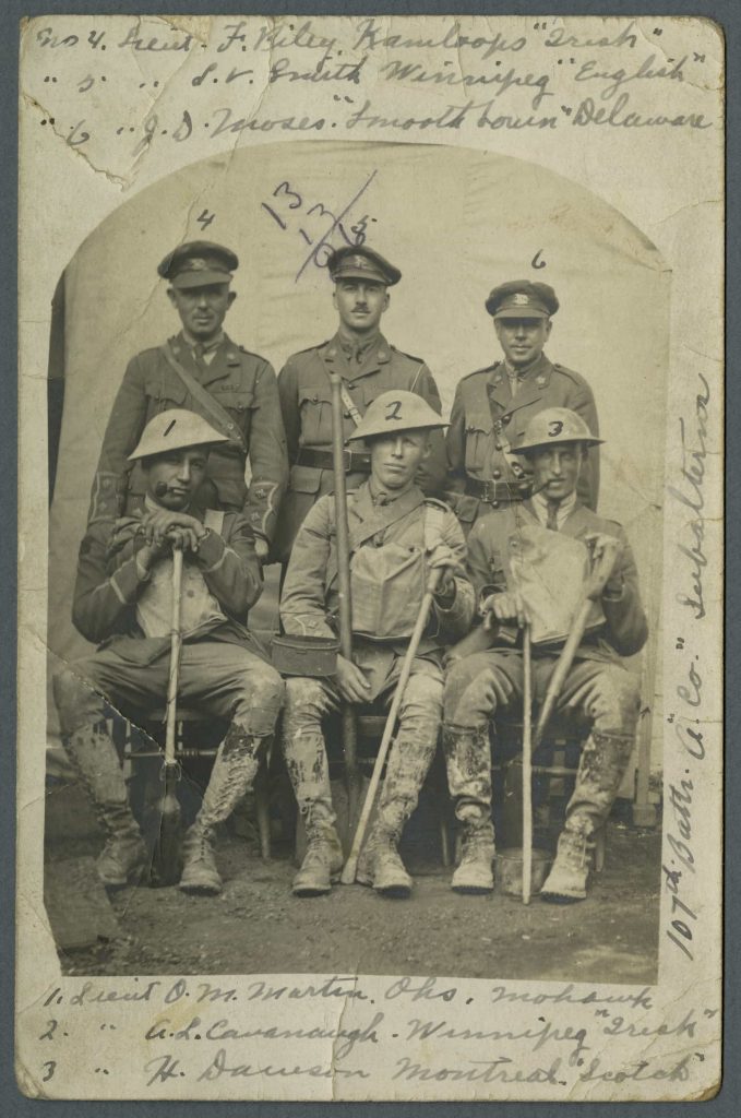Trois hommes en uniforme se tiennent derrière trois autres assis, aux uniformes tachés de boue et tenant des pelles et des bâtons de marche. Tous sont identifiés par des numéros et un court texte.