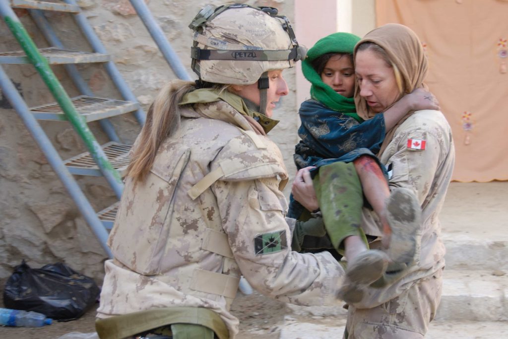Une femme en uniforme porte une enfant afghane dans ses bras, assistée par une autre femme en uniforme.