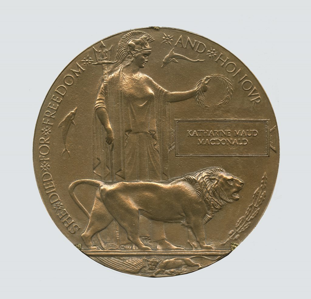 Un disque en bronze gravé à la figure de Britannia tenant une couronne d’olivier et un trident, et accompagnée d’un lion et de deux dauphins. Les personnages sont entourés des mots “She died for freedom and honour” (Elle est morte pour la liberté et l’honneur). Le nom de Katherine Maud Macdonald est inscrit sur le côté droit.