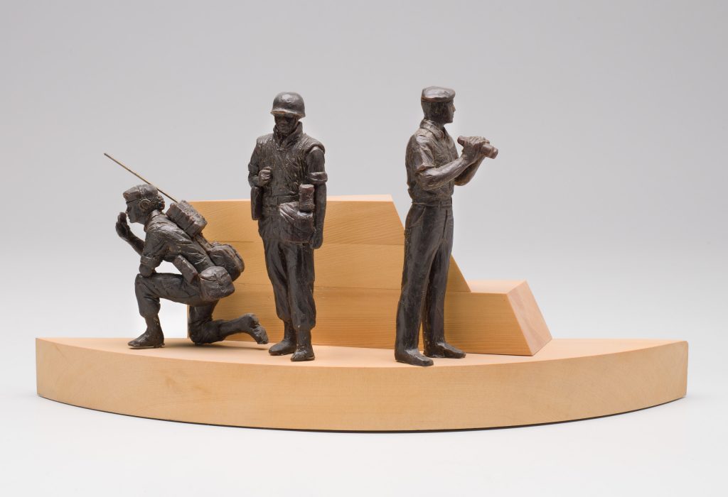 Trois petits personnages en uniforme de couleur sombre, deux hommes debout et une femme un genou à terre, observent depuis une plateforme en bois à plusieurs niveaux