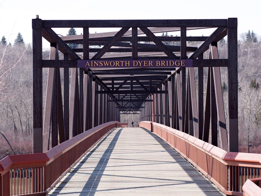 L’entrée d’un pont à fermes avec une plaque près du sommet de la structure portant le nom du pont en anglais : Ainsworth Dyer Bridge.