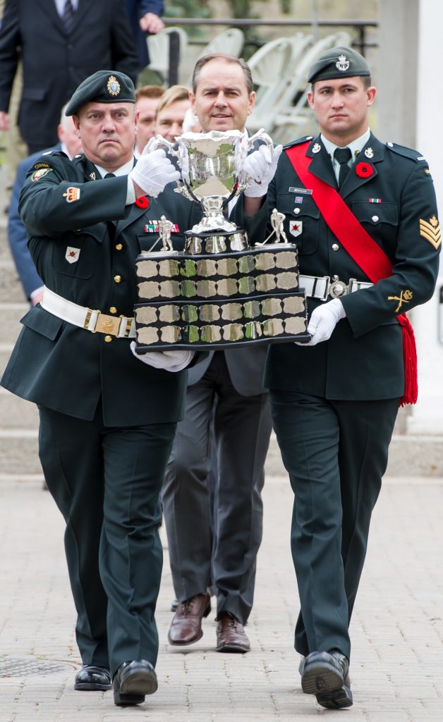 Une procession menée par deux soldats en uniforme arborant un coquelicot sur leur revers et portant la coupe Memorial.