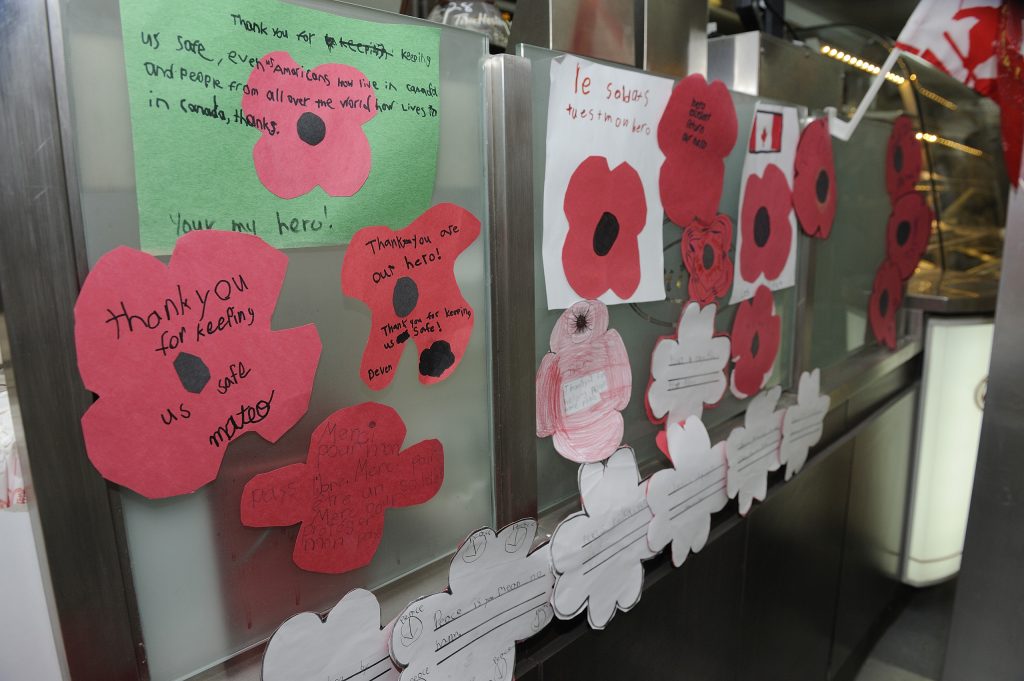 Des coquelicots en papier et des messages de remerciements manuscrits en français et en anglais ornent la vitre hygiénique du comptoir de service d’un restaurant Tim Hortons.