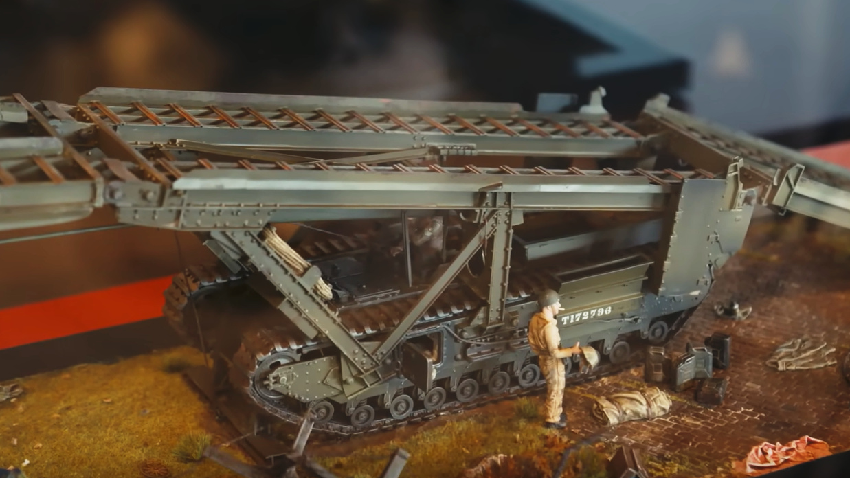 Modèle réduit d’un grand pont métallique pliant en trois parties, monté sur un véhicule militaire à chenilles.