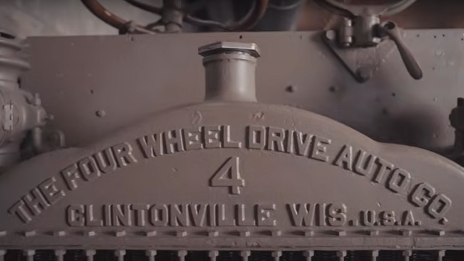 Gros plan sur l’avant d’un vieux camion gris en métal portant l’inscription « The Four Wheel Drive Auto Co, Clintonville, Wis, U.S.A. »