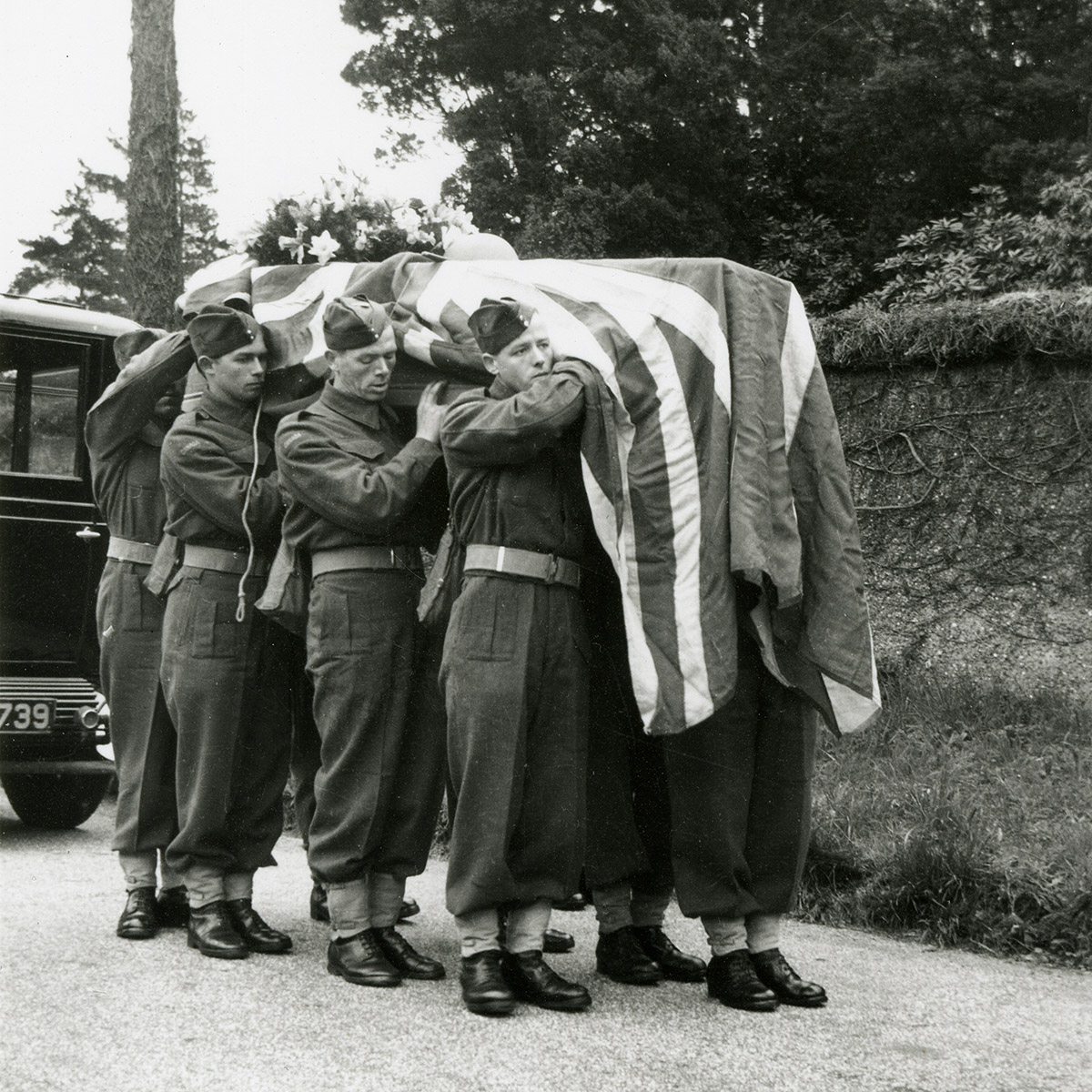 Photo de huit militaires portant sur leurs épaules un cercueil couvert d’un drapeau.
