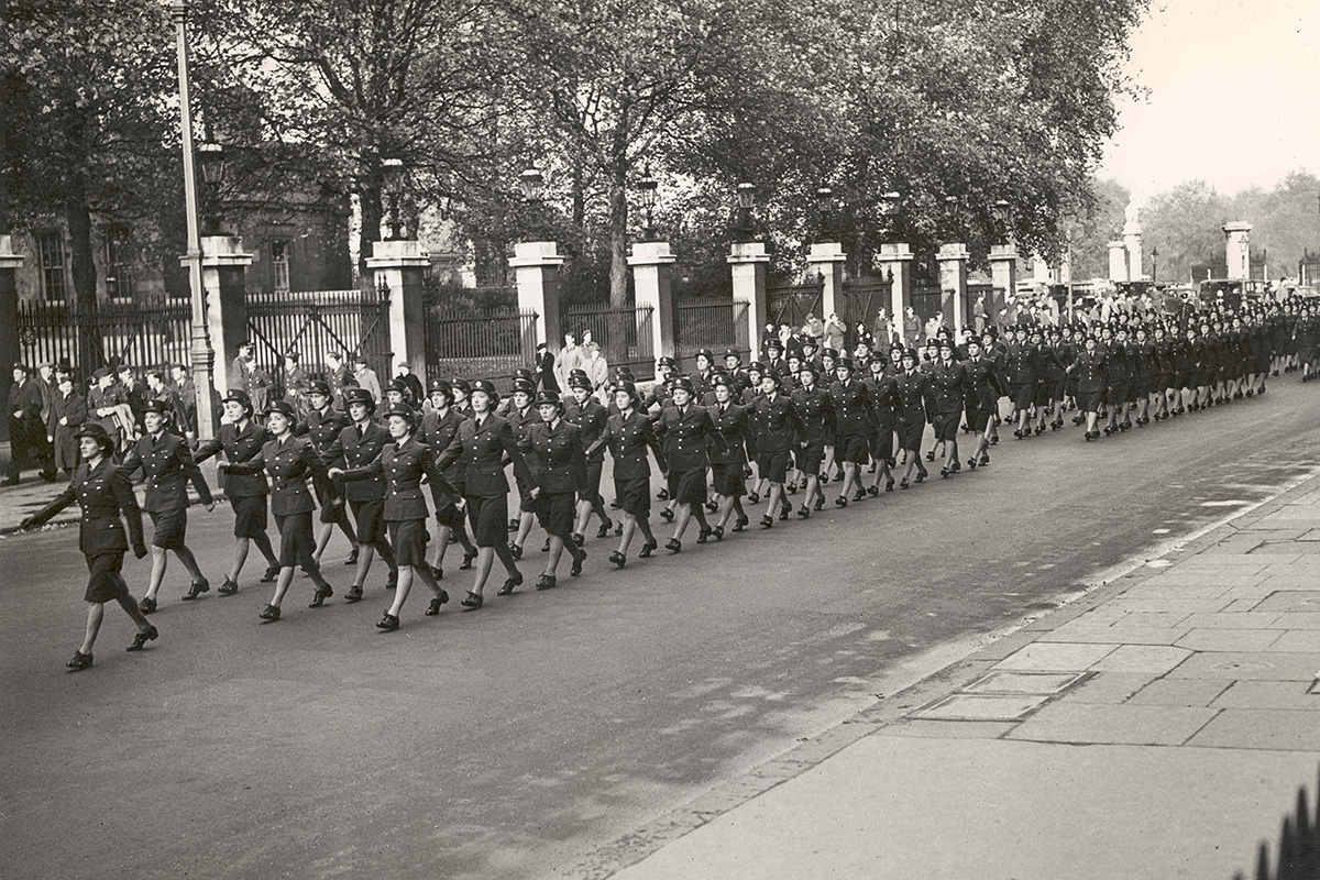 Photographie d’un défilé de femmes en uniforme descendant la rue, de droite à gauche.