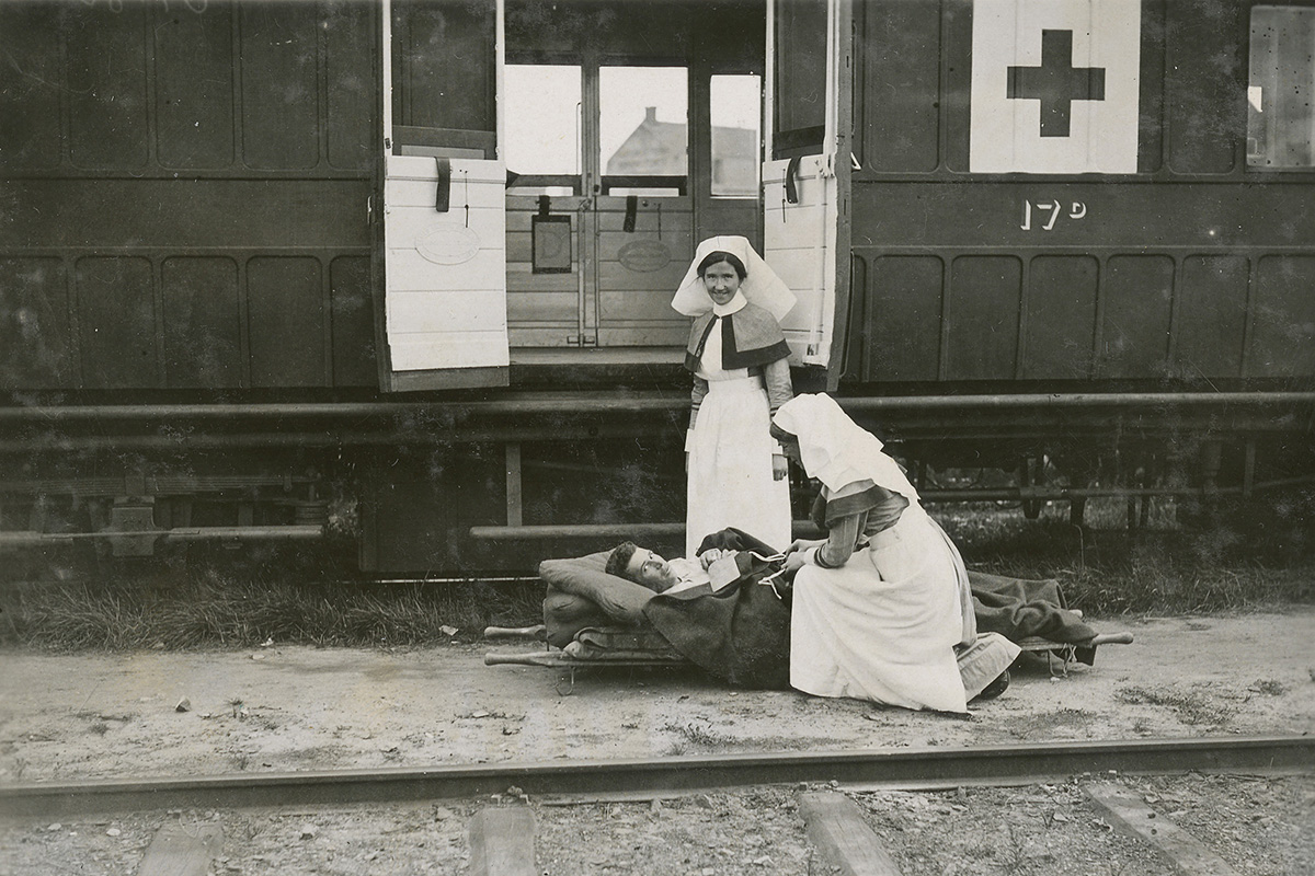 Photographie de deux infirmières devant un train-hôpital s’occupant d’une personne sur un brancard.
