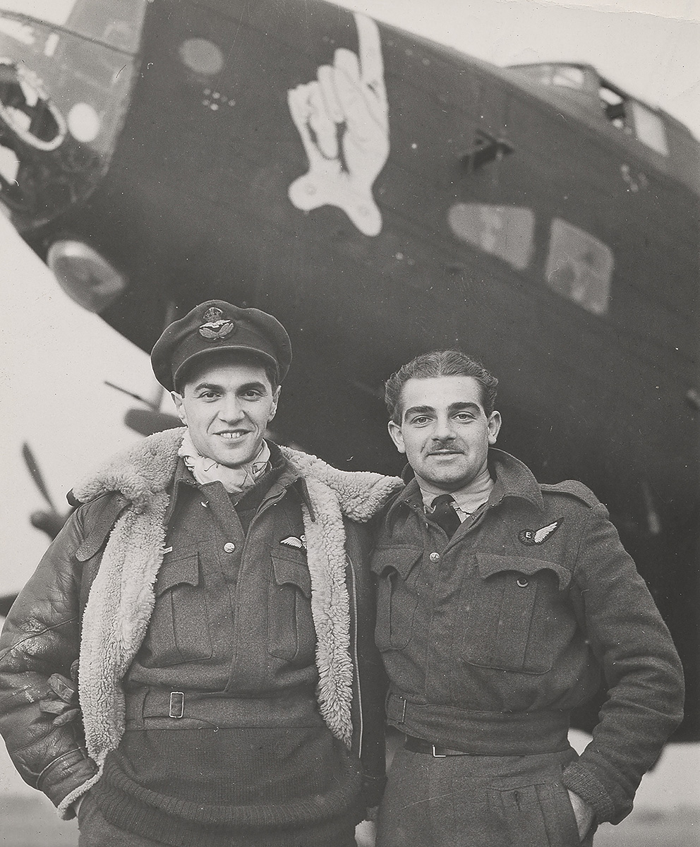 Photographie de deux membres d’équipage se tenant debout devant le nez d’un bombardier Halifax.