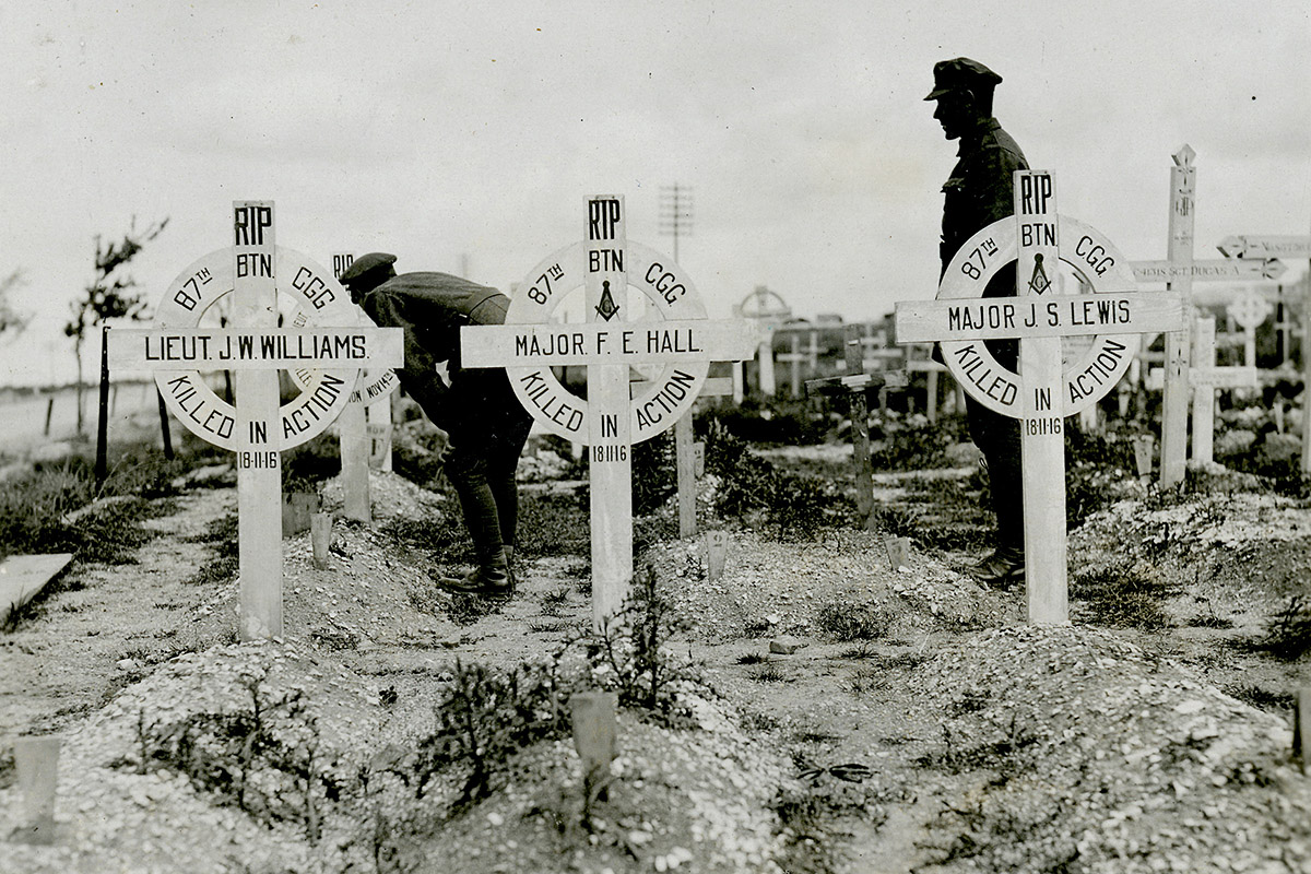 Photographie de soldats observant des tombes avec des pierres tombales à croix blanche.