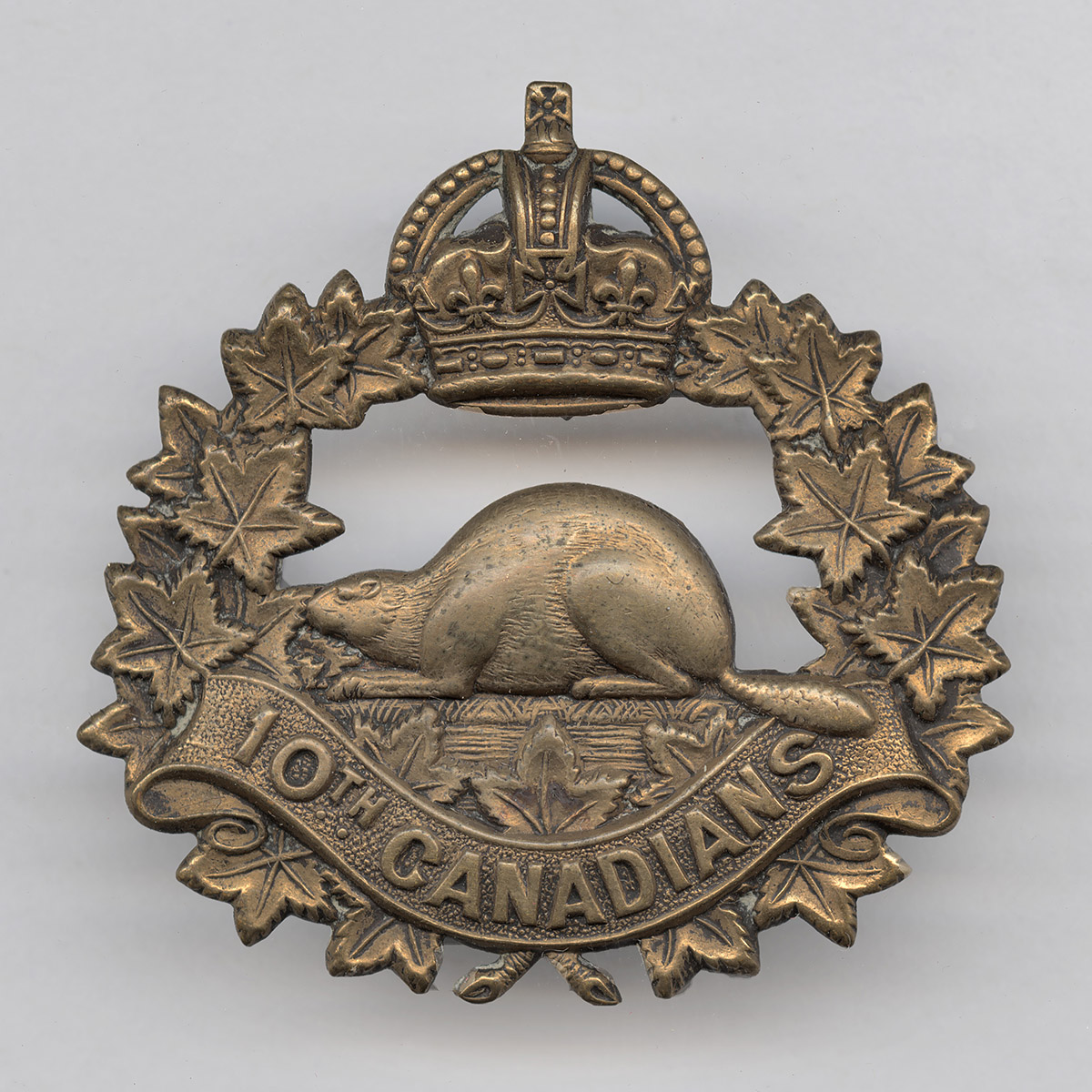 Insigne de casquette en métal avec une couronne de feuilles d’érable, une couronne Tudor au sommet et un castor au milieu. On peut y lire l’inscription suivante, en anglais : « 10e Canadiens ».