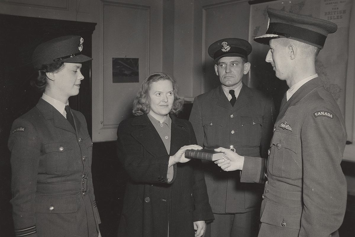 Photographie d’une femme ayant la main tendue sur un livre, avec deux personnes en uniforme à ses côtés. Une troisième personne en uniforme tient le livre.