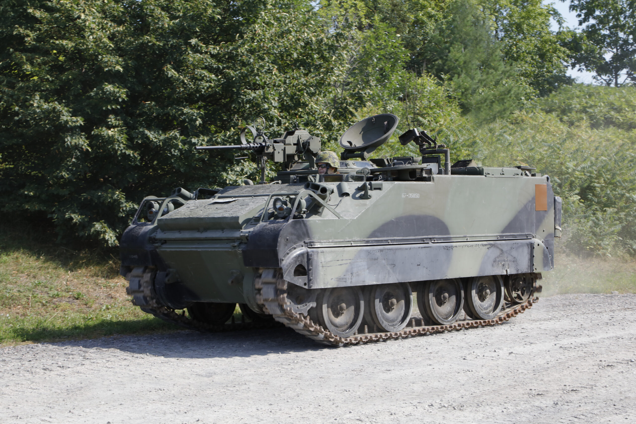 A tracked armoured vehicle in green, brown and black camouflage, with a communications dish antenna and a machine gun on top.