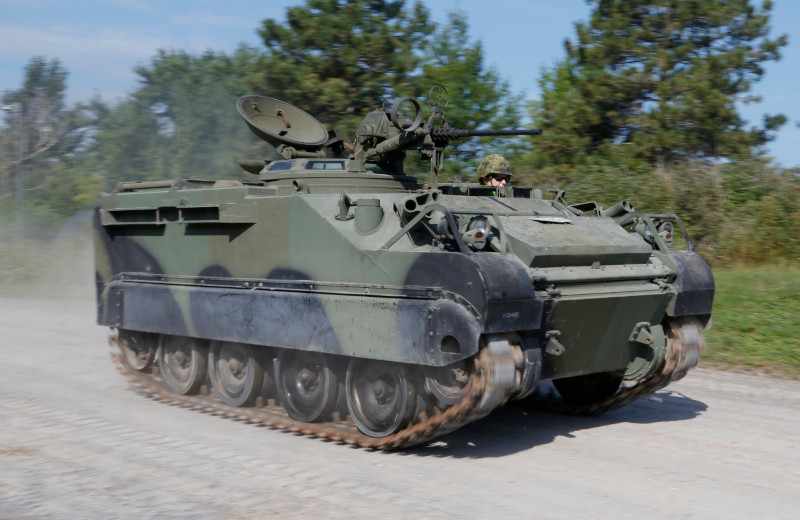 A tracked armoured vehicle in green, brown and black camouflage, with a communications dish antenna and a machine gun on top.
