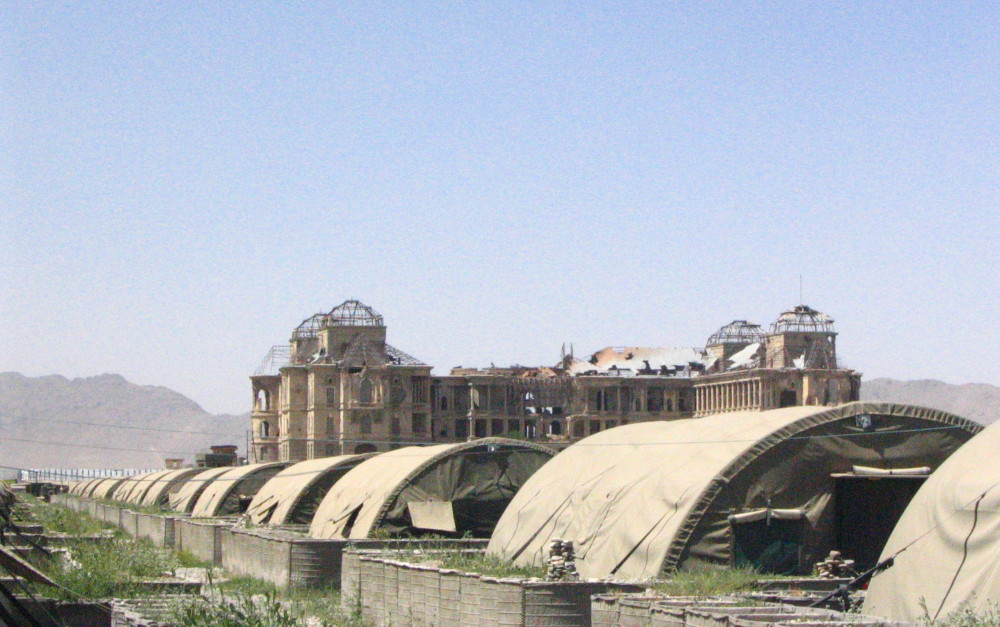 Une longue rangée de structures ressemblant à des tentes aux toits incurvés, avec un grand bâtiment en ruines en arrière-plan.