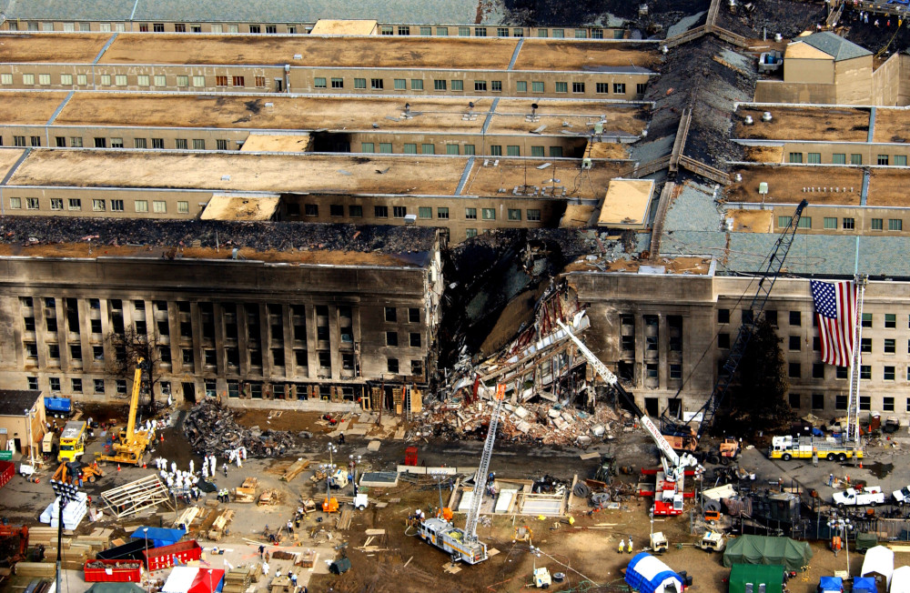 Vue aérienne d’un grand bâtiment endommagé et incendié, avec de nombreux véhicules de chantier à l’avant-plan.
