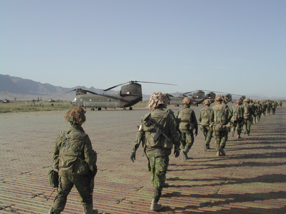 Une longue file de militaires portant des uniformes de camouflage verts se dirige vers plusieurs gros hélicoptères.