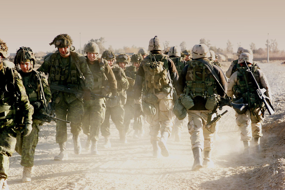 Un groupe de militaires vêtus d’uniformes de camouflage verts s’avance vers la caméra, croisant un autre groupe de militaires en uniformes de camouflage beige qui marche dans la direction opposée.