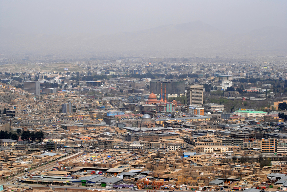 Un paysage urbain varié occupe tout le cadre, comprenant de vastes zones de bâtiments bas, des groupes d’immeubles d’habitation, quelques édifices administratifs et religieux, ainsi que des espaces verts.