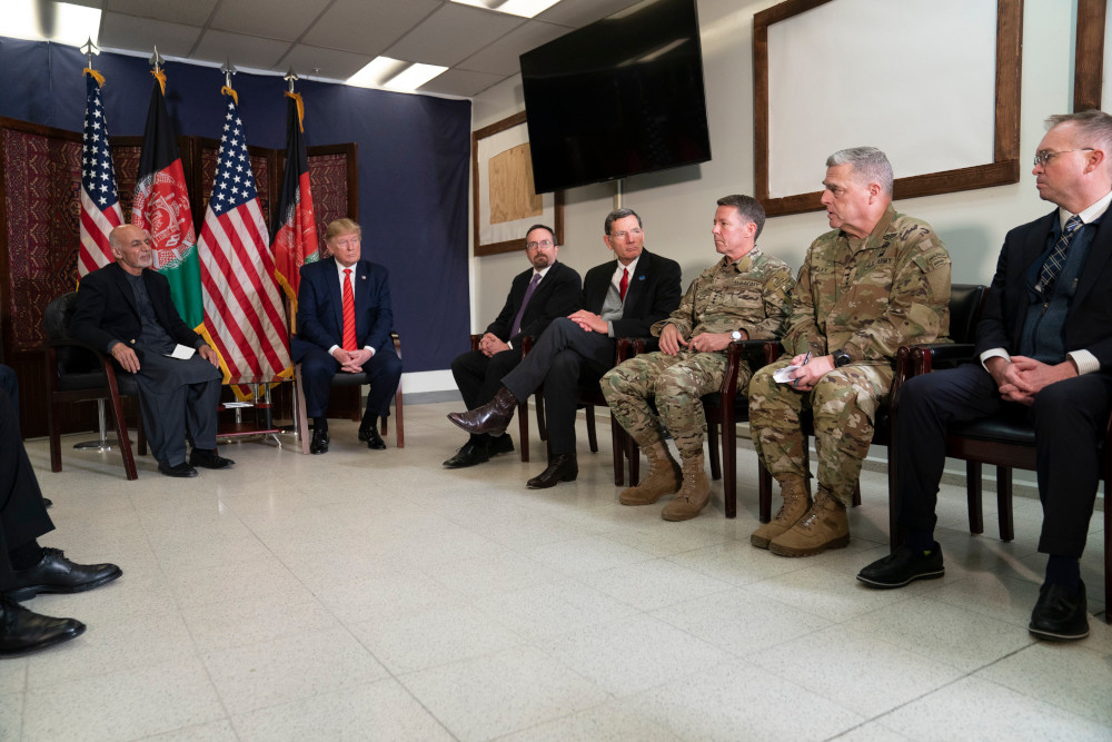 Plusieurs hommes, certains en uniforme militaire et d’autres en complets, sont assis sur des chaises disposées tout autour d’une pièce.