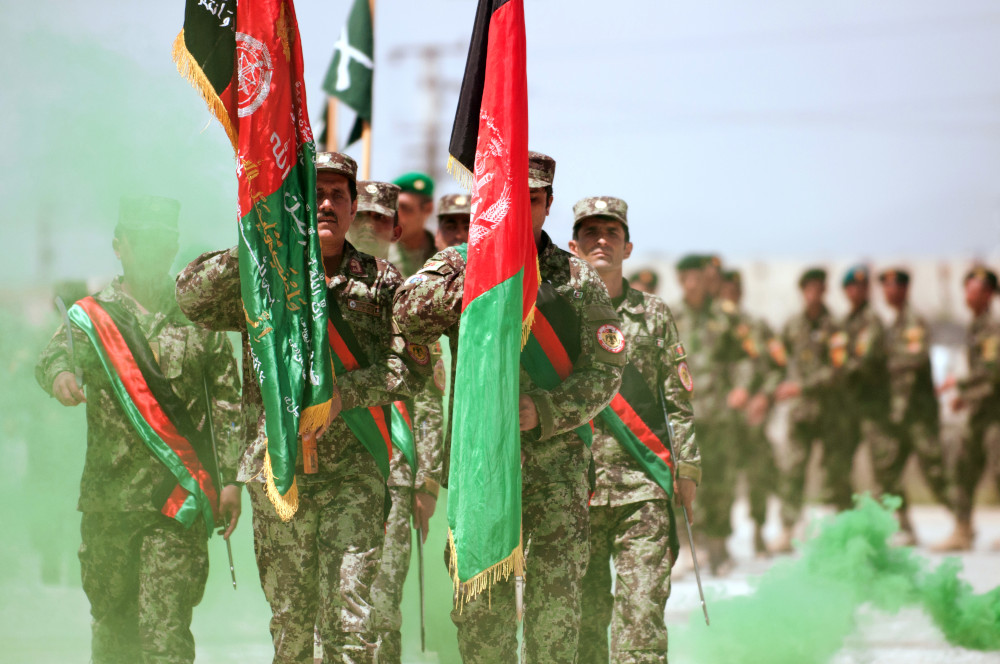 Un groupe de personnes à la peau de teint moyen, vêtues d’uniformes de camouflage, défilent en brandissant des drapeaux afghans.
