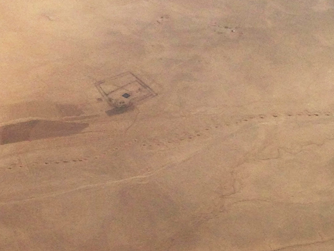 Photo aérienne d’un paysage aride montrant une route et d’autres structures régulières, des lits de rivières sinueux et une série de points en ligne sur toute la largeur de la photo.