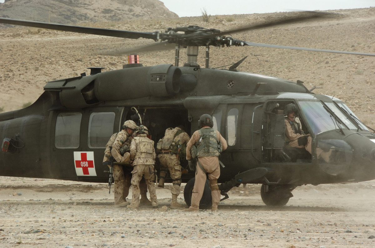 Un groupe de militaires portant des tenues de camouflage beige monte à bord d’un hélicoptère vert foncé affichant une croix rouge.