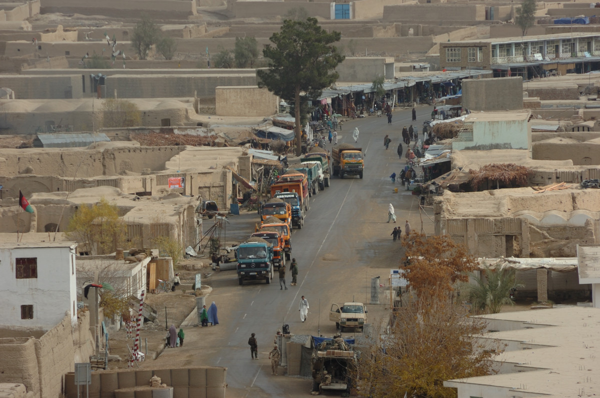 Une rue bordée de bâtiments bas, de véhicules et de gens.