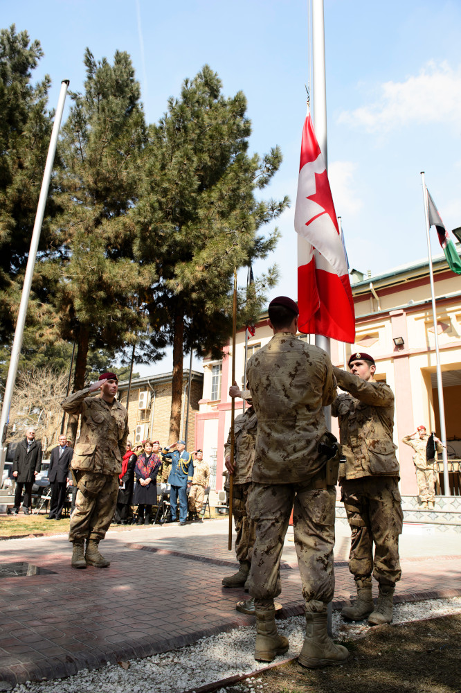 Deux soldats baissent un drapeau canadien tandis qu’un troisième soldat salue.