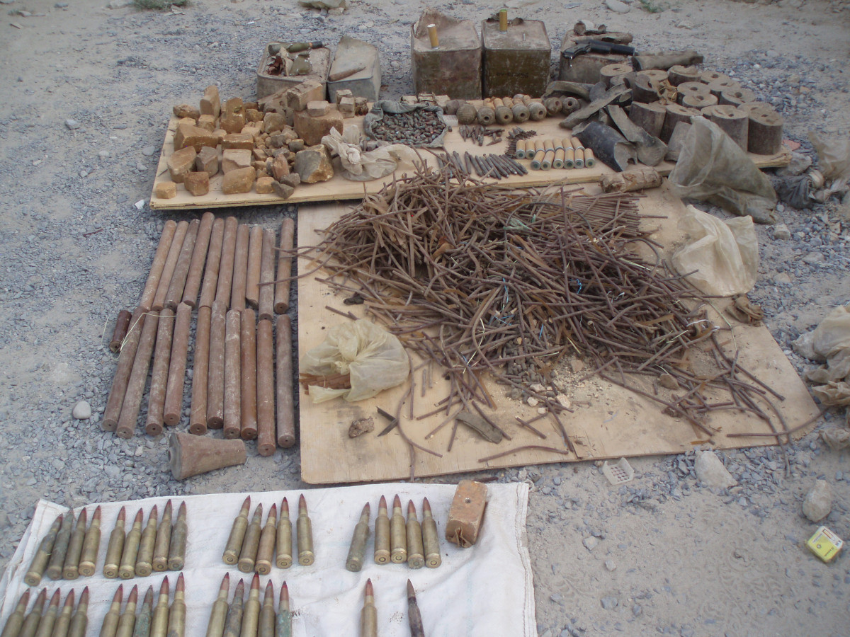 Un amoncèlement de munitions et de morceaux de métal de différentes tailles, éparpillés sur le sol, sur des planches de bois et des morceaux de tissu.